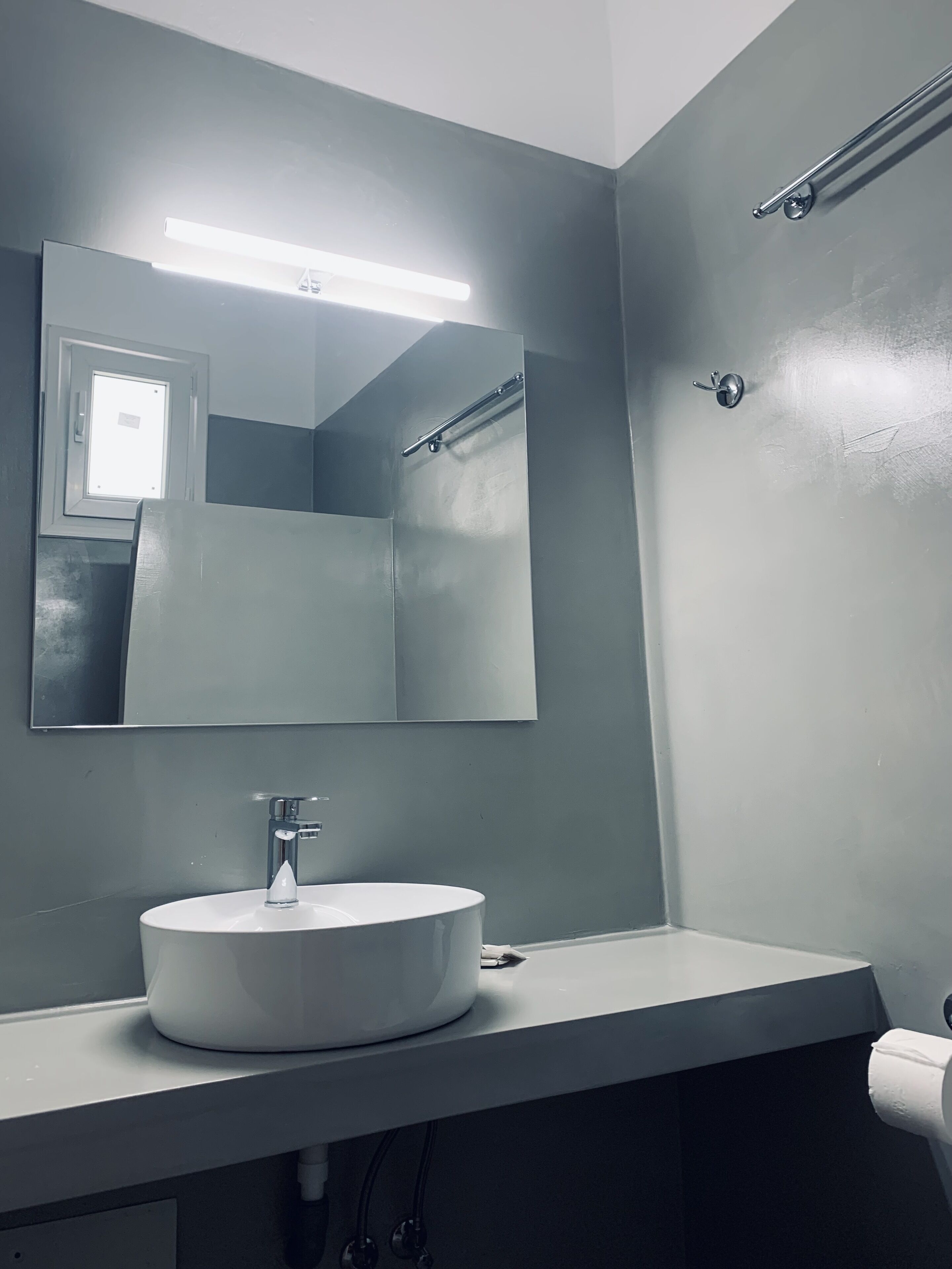 A modern bathroom with a white sink, a large mirror, and a towel rack.