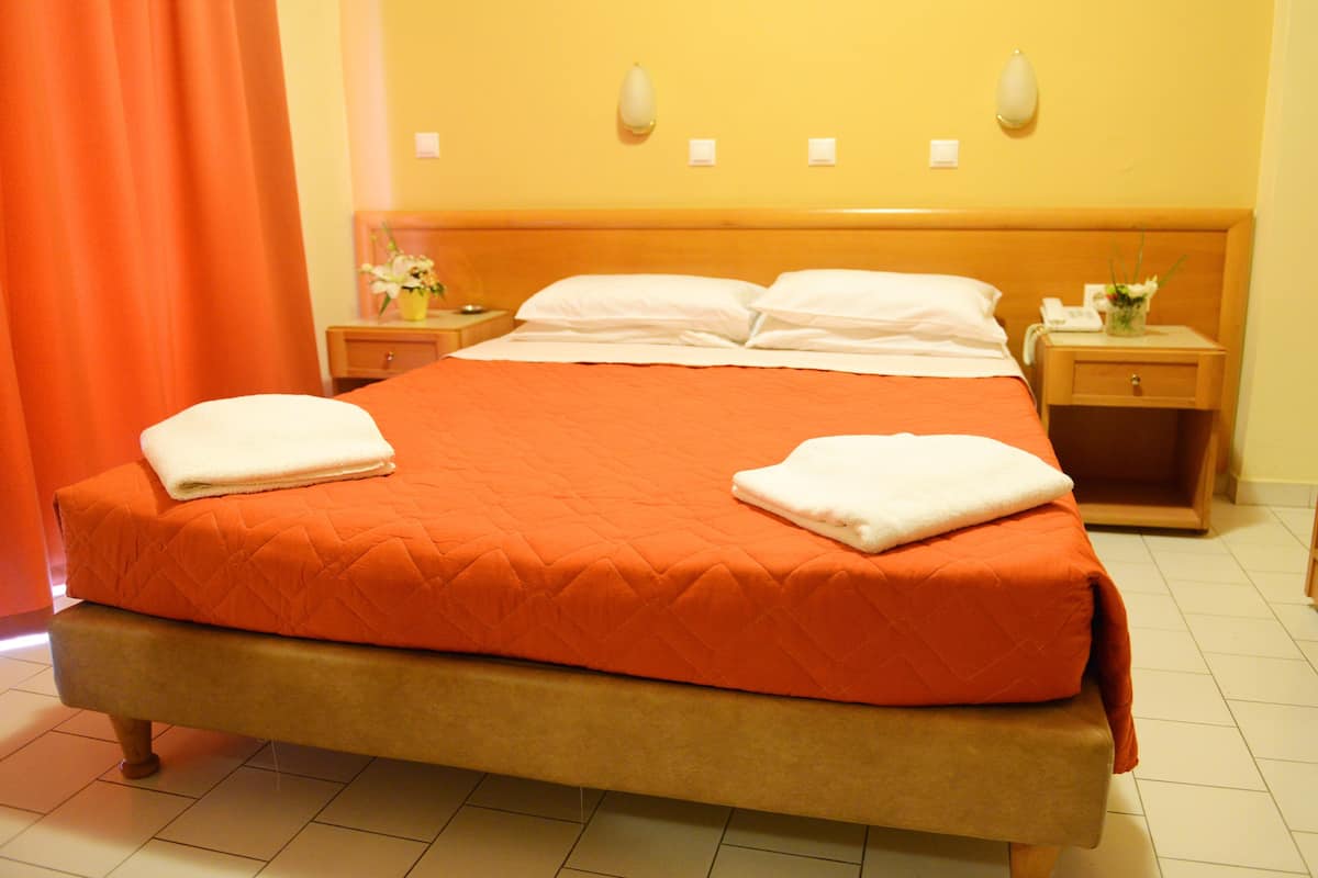 Una cama con un edredón naranja, dos almohadas blancas y una manta blanca a un lado.