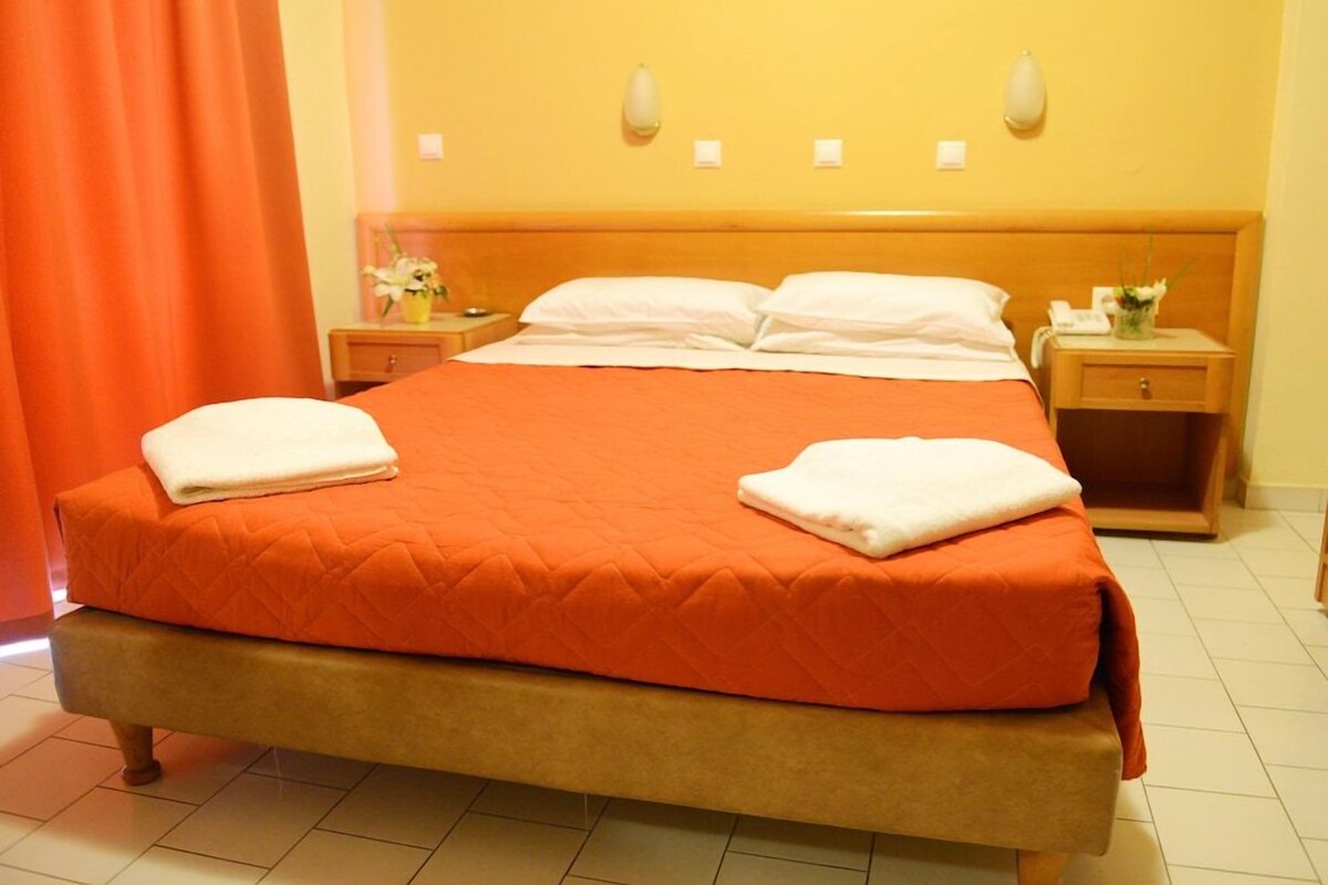 A hotel room with a large bed, orange bedding, two bedside tables with lamps, and a mirror on the wall.