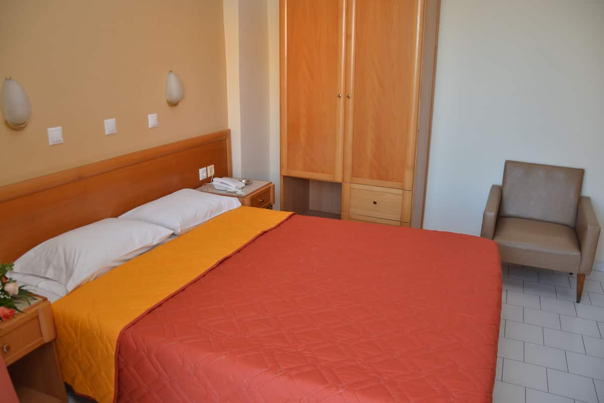 Habitación de hotel con una cama grande, un armario de madera, una silla y una mesita de noche con un teléfono y un arreglo floral.