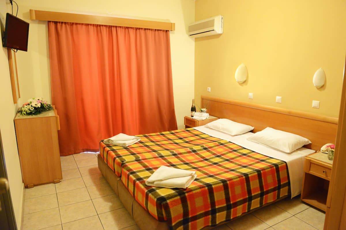 Habitación de hotel con cama, mesita de noche, escritorio, silla, televisor y ventana con cortinas.