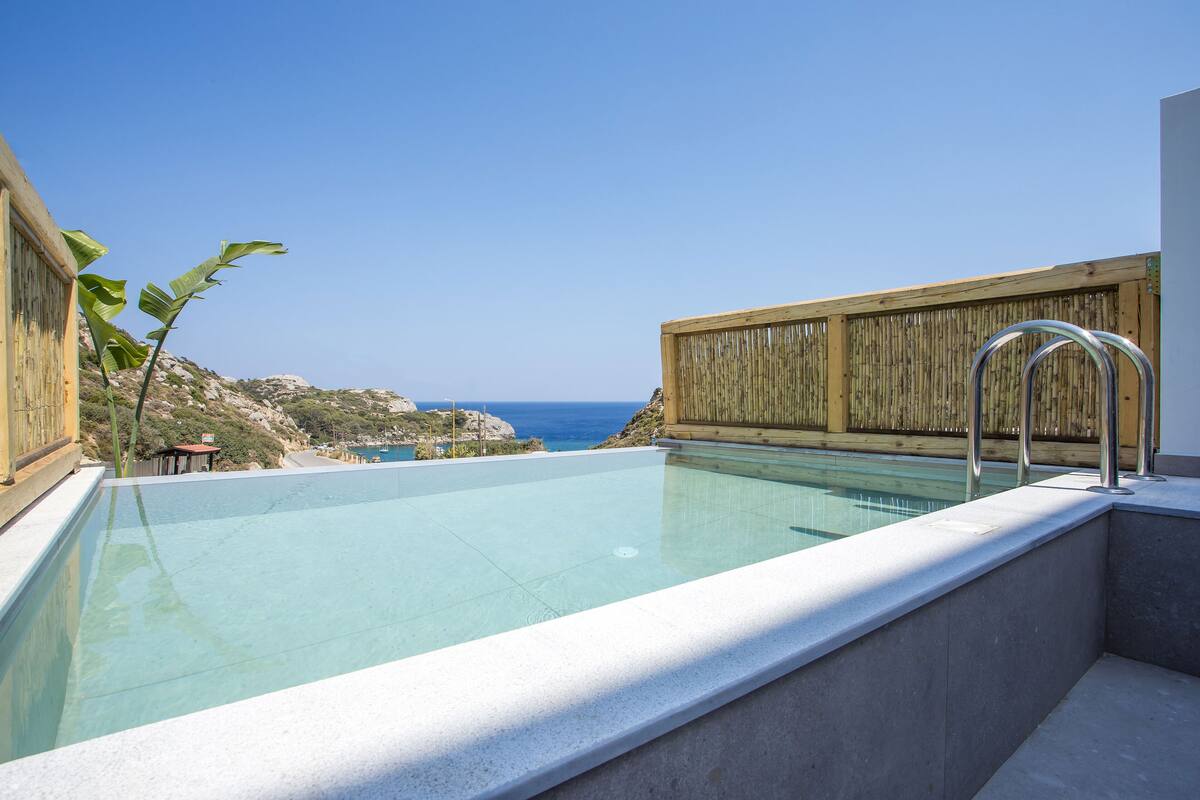 Une piscine aux eaux cristallines, entourée d’une clôture en bois, et offrant une vue sur la mer.