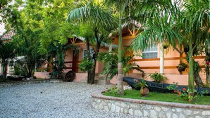 A courtyard with a stone pathway, palm trees, and a building with a peach facade. - Palm Inn Hotel (Port-au-Prince)