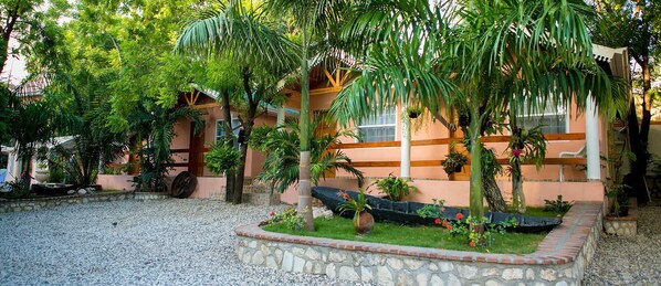 A courtyard with a stone pathway, palm trees, and a building with a peach facade. - Palm Inn Hotel (Port-au-Prince)