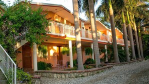 A two-story building with a balcony, surrounded by palm trees and a gravel driveway. - Palm Inn Hotel (Port-au-Prince)