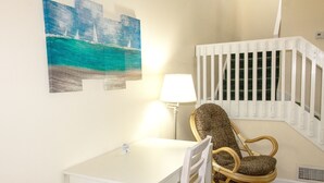 A small room with a white table and chair, a lamp, a painting of a sailboat, and a white railing. - Deercreek Townhomes (Surfside Beach)