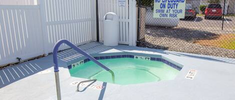 A swimming pool with a no lifeguard on duty sign, a fence, and a trash can.