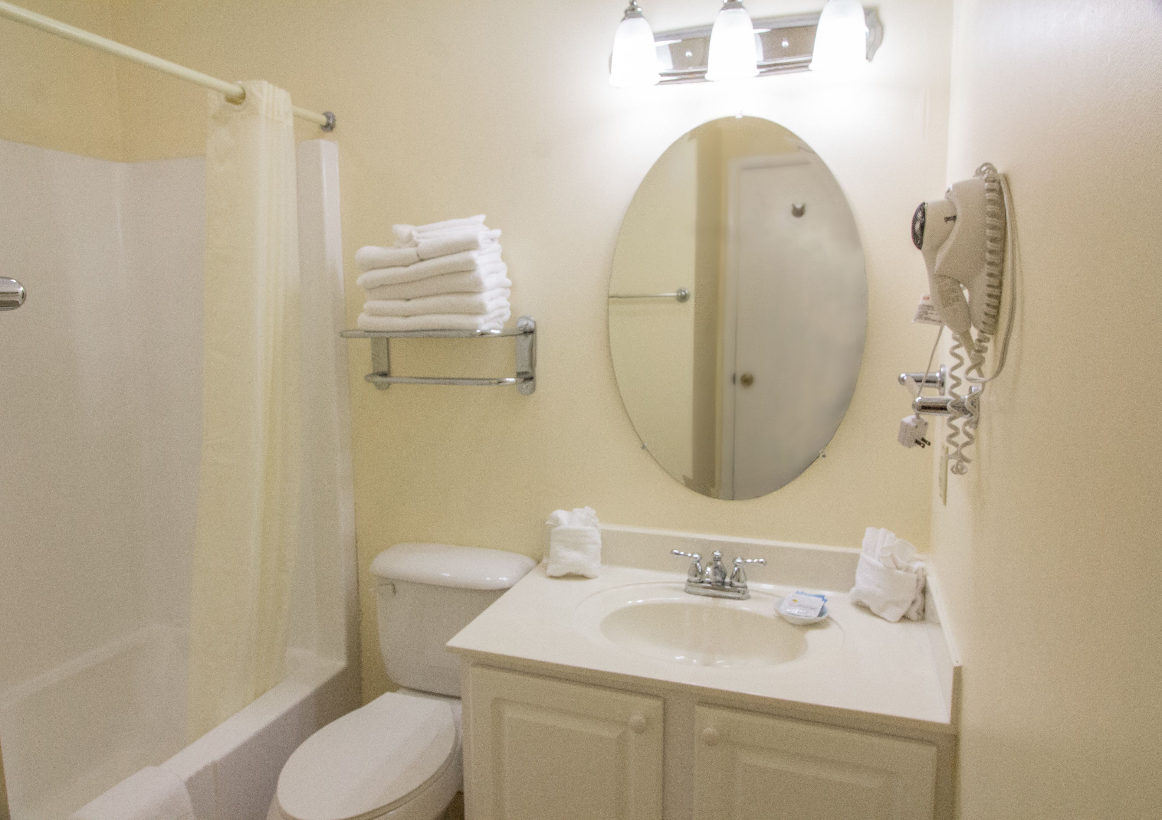 Un baño con inodoro, lavabo y ducha. Hay toallas en un estante y un secador de pelo en la pared.