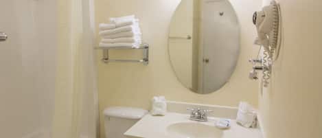 Un baño con inodoro, lavabo y ducha. Hay toallas en un estante y un secador de pelo en la pared.