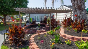 A garden with a wooden pergola, a brick fire pit, and various plants and flowers. - Deercreek Townhomes (Surfside Beach)