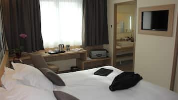 Habitación de hotel con cama, escritorio, silla, televisión y espejo de baño.