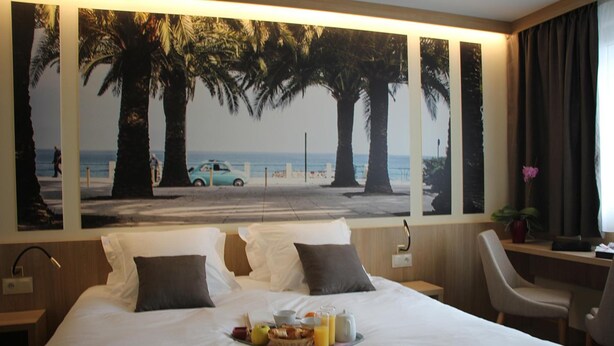 Habitación de hotel con cama, bandeja de desayuno, escritorio, silla y un mural grande con temática de playa.