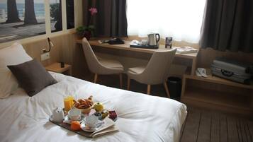 Une chambre d’hôtel équipée d’un lit, d’un plateau de petit-déjeuner, d’un bureau, de chaises et d’une fenêtre donnant sur des palmiers et la mer.