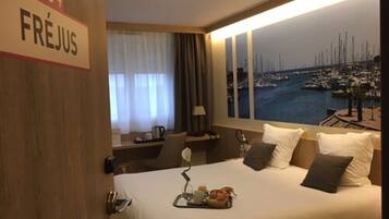 Habitación de hotel con cama, escritorio, ventana y vista al puerto deportivo, además de un cartel que indica el número 204.