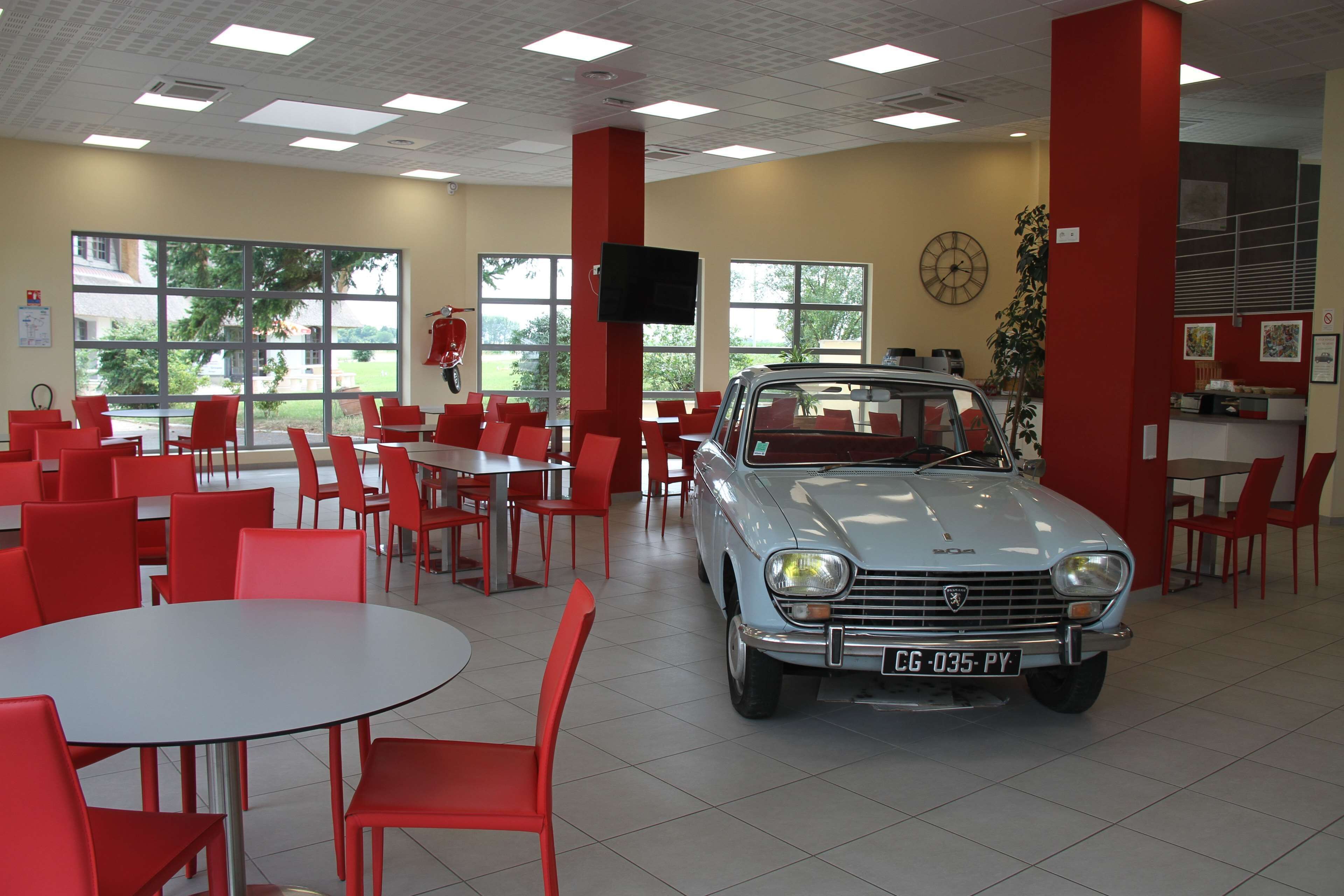 A car showroom with a vintage car, red chairs, and tables.