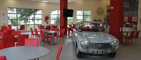 A car showroom with a vintage car, red chairs, and tables.