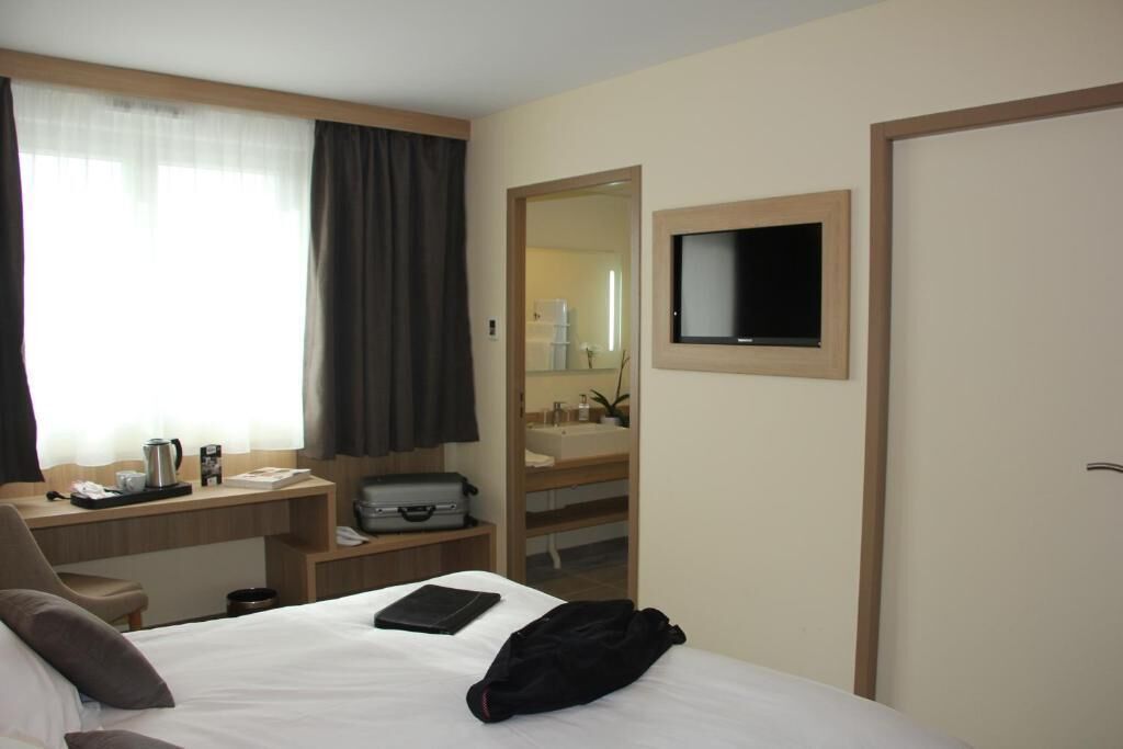 Habitación de hotel con cama, escritorio con computadora, espejo y televisión.