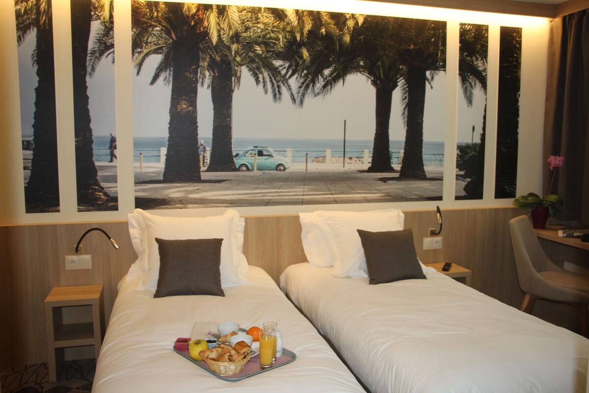 A hotel room with two beds, a breakfast tray, and a beach view mural.