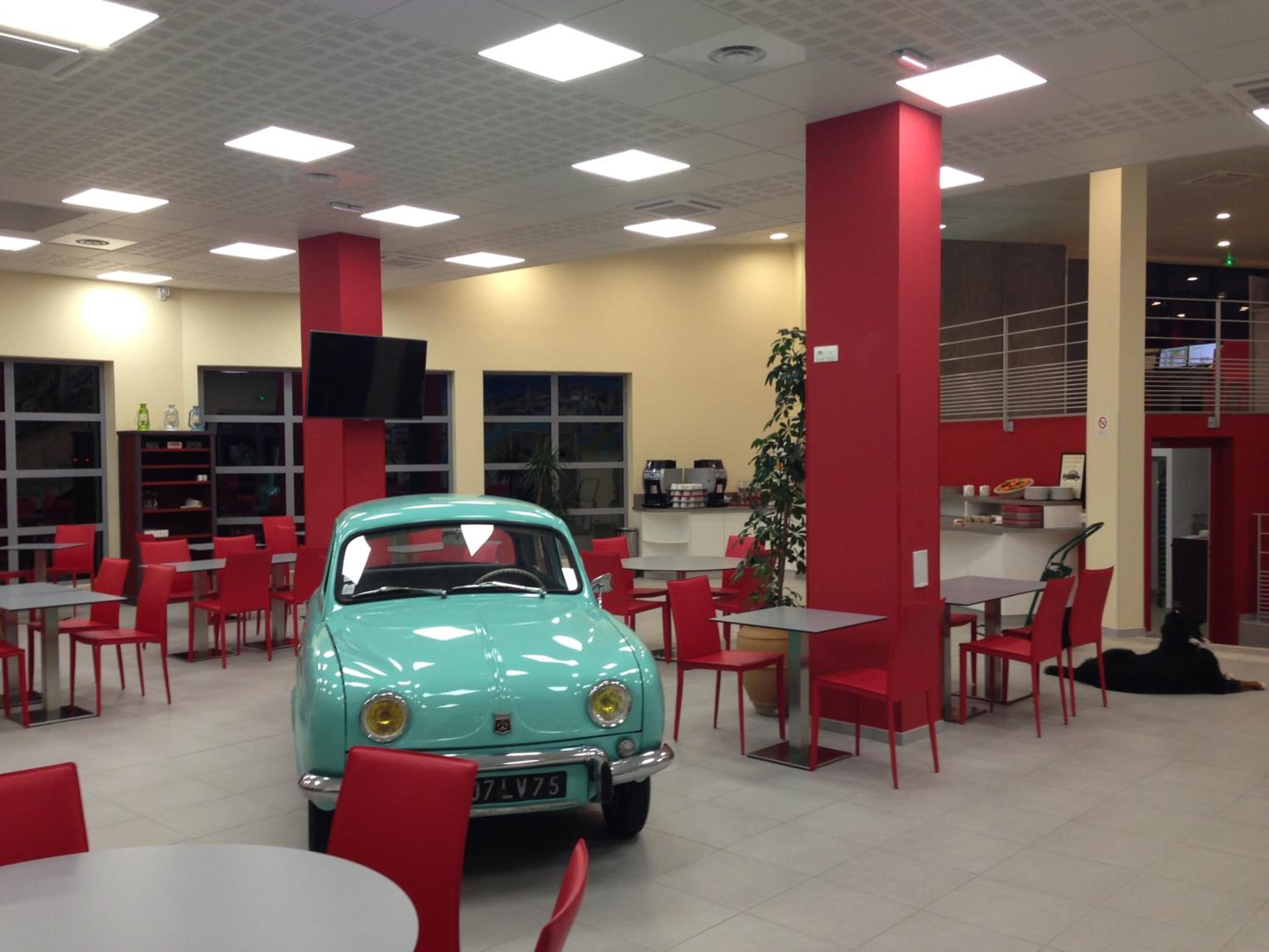 A dining area with red chairs and tables, a turquoise vintage car, and a large plant.