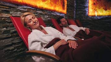 Two people relaxing in a spa-like setting with stone walls and fire elements.