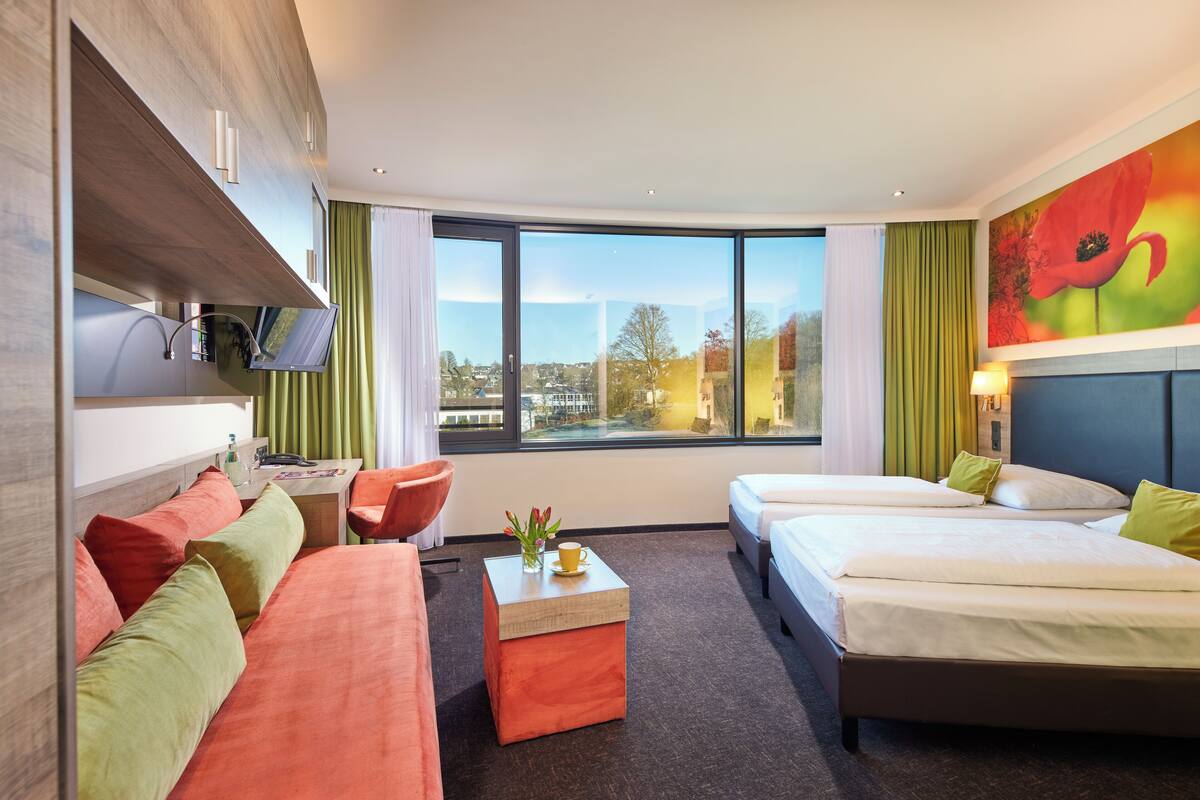 A hotel room with two beds, a sofa, a small table, and a TV.