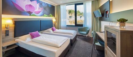 Une chambre d’hôtel avec deux lits, un bureau, une chaise, une télévision et une grande fenêtre avec des rideaux.