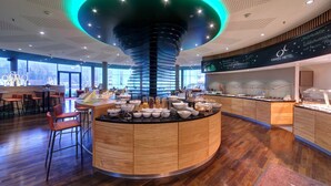 A modern hotel lobby with a central island counter, wooden flooring, and a ceiling with a unique spiral design. - HANSE HOTEL Attendorn (Attendorn)