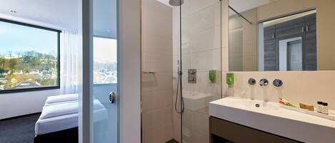 Un baño de hotel moderno con ducha de vidrio, un espejo grande y un lavabo blanco.