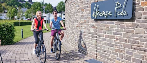 Two people riding bicycles on a paved path in front of a building with a sign that reads "Hanse Pub".