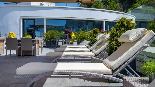 A modern outdoor lounge area with wicker lounge chairs and a glass-enclosed dining area. - HANSE HOTEL Attendorn (Attendorn)