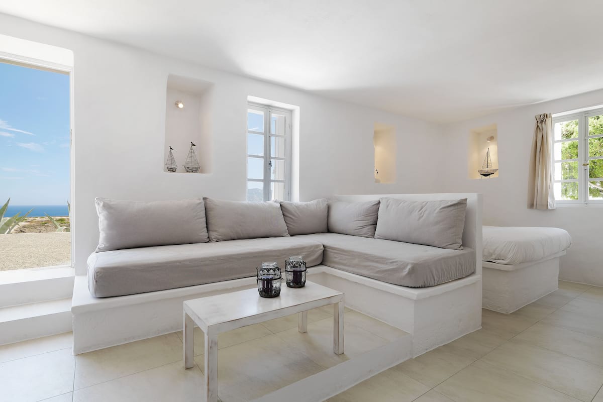 A modern living room with a beige sectional sofa, a white coffee table, and a view of the beach.