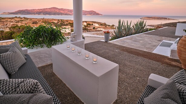 A terrace with a white sofa, a table with candles, and a view of the sea and hills. - The Windmill Kimolos (Kimolos)