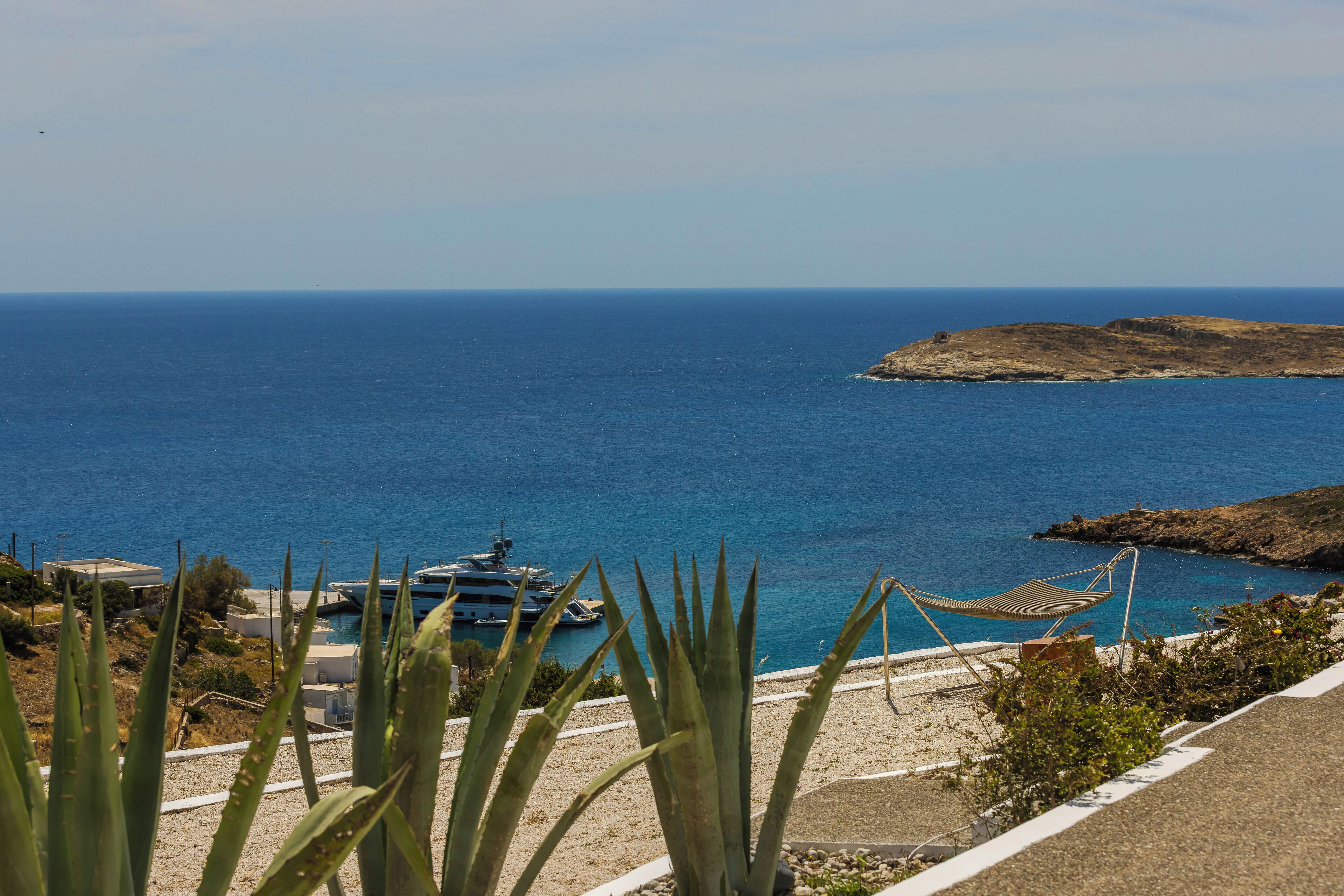 A coastal view with a hammock, a boat, and a rocky island.