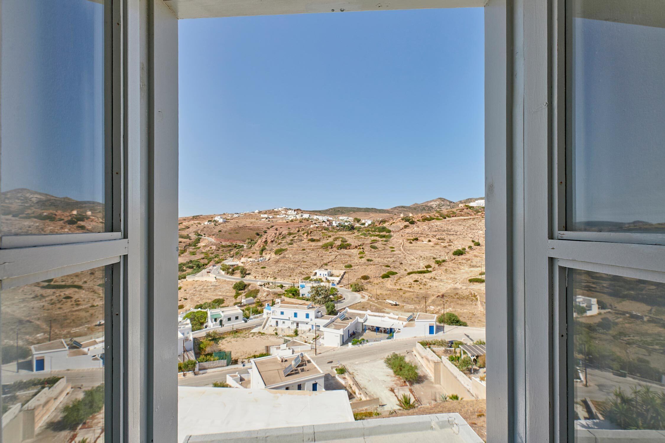 A view from a window overlooking a small town with buildings and hills in the background.