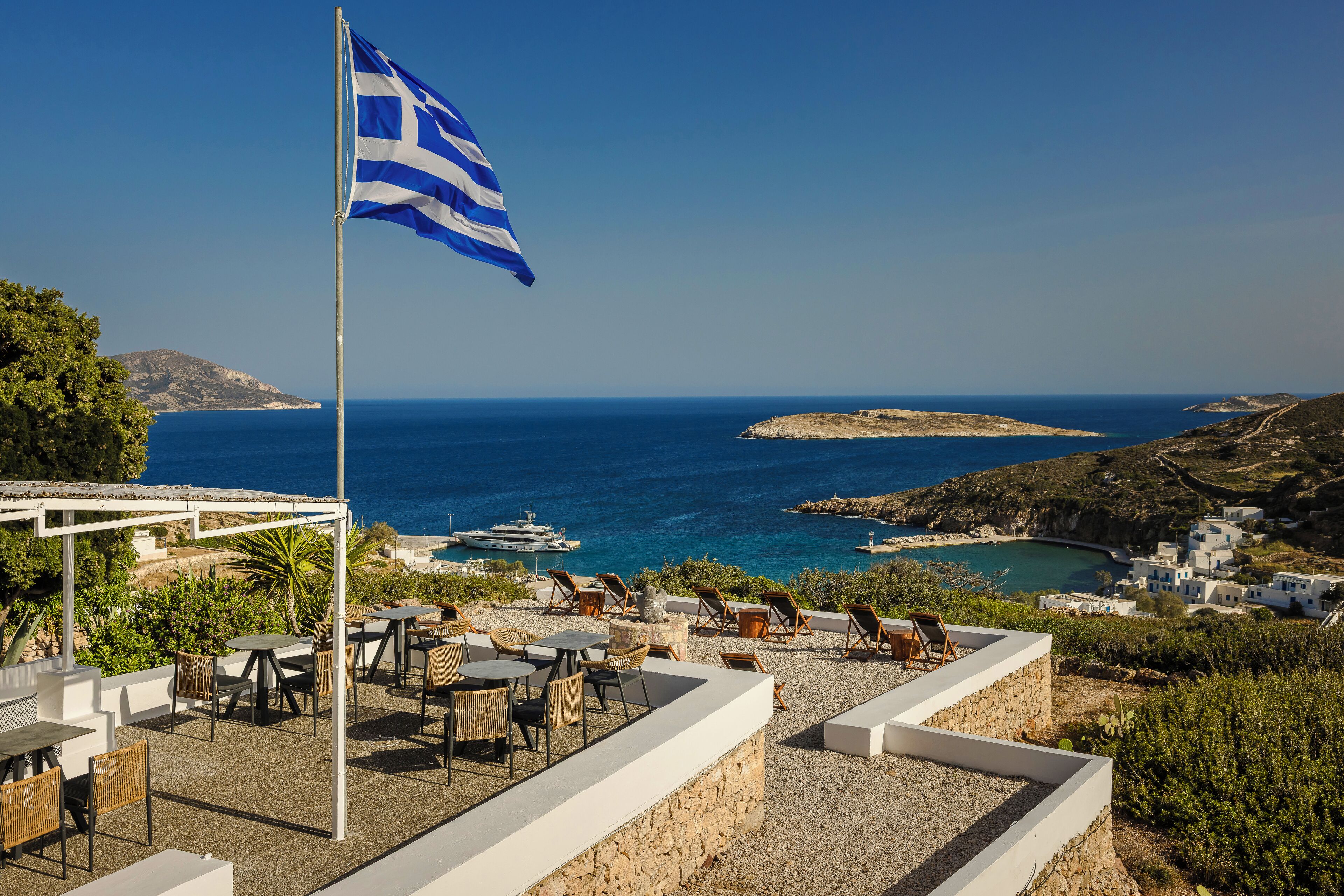 A terrace with outdoor seating, a flag, and a view of the sea and coastline.