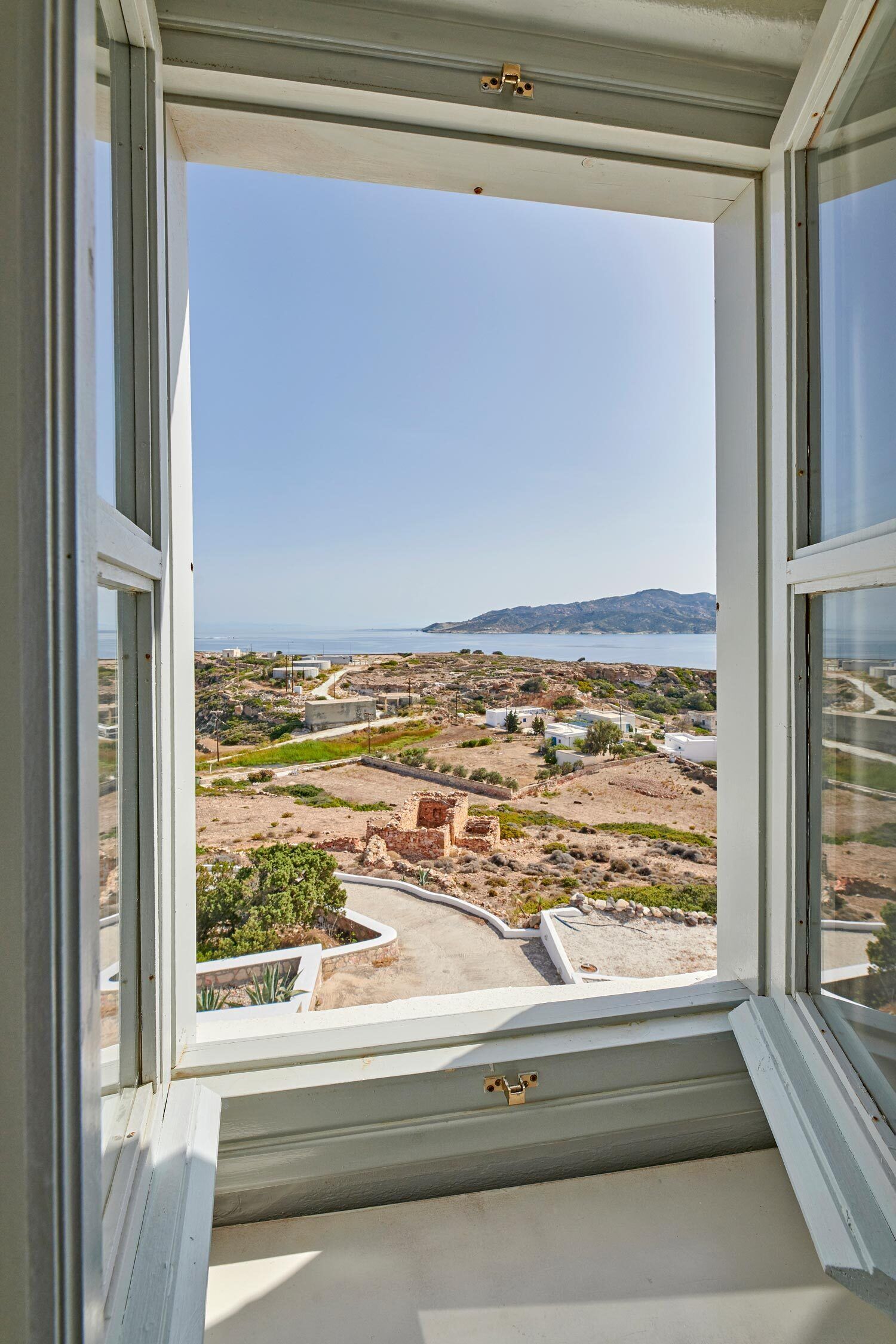 A view from a window overlooking a coastal landscape with buildings and a clear sky.