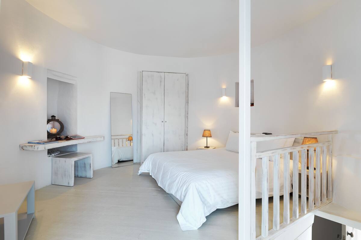 A bedroom with a bed, a nightstand, a mirror, a wardrobe, and a small desk with a lamp.