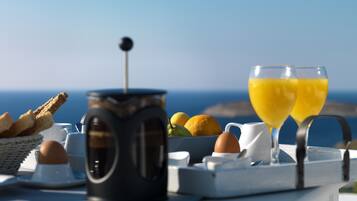 A breakfast setup with a coffee pot, eggs, toast, and orange juice glasses on a table with a scenic ocean view in the background.