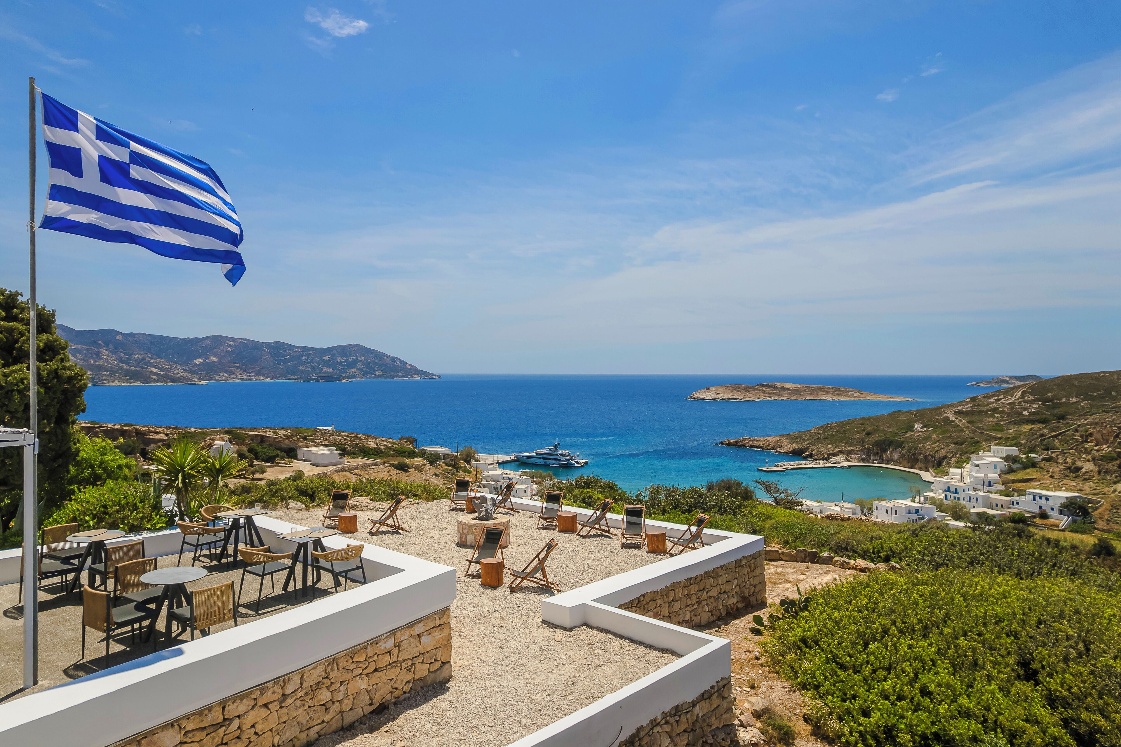 A terrace with outdoor seating overlooking a coastal landscape, a flag, and a view of the sea.