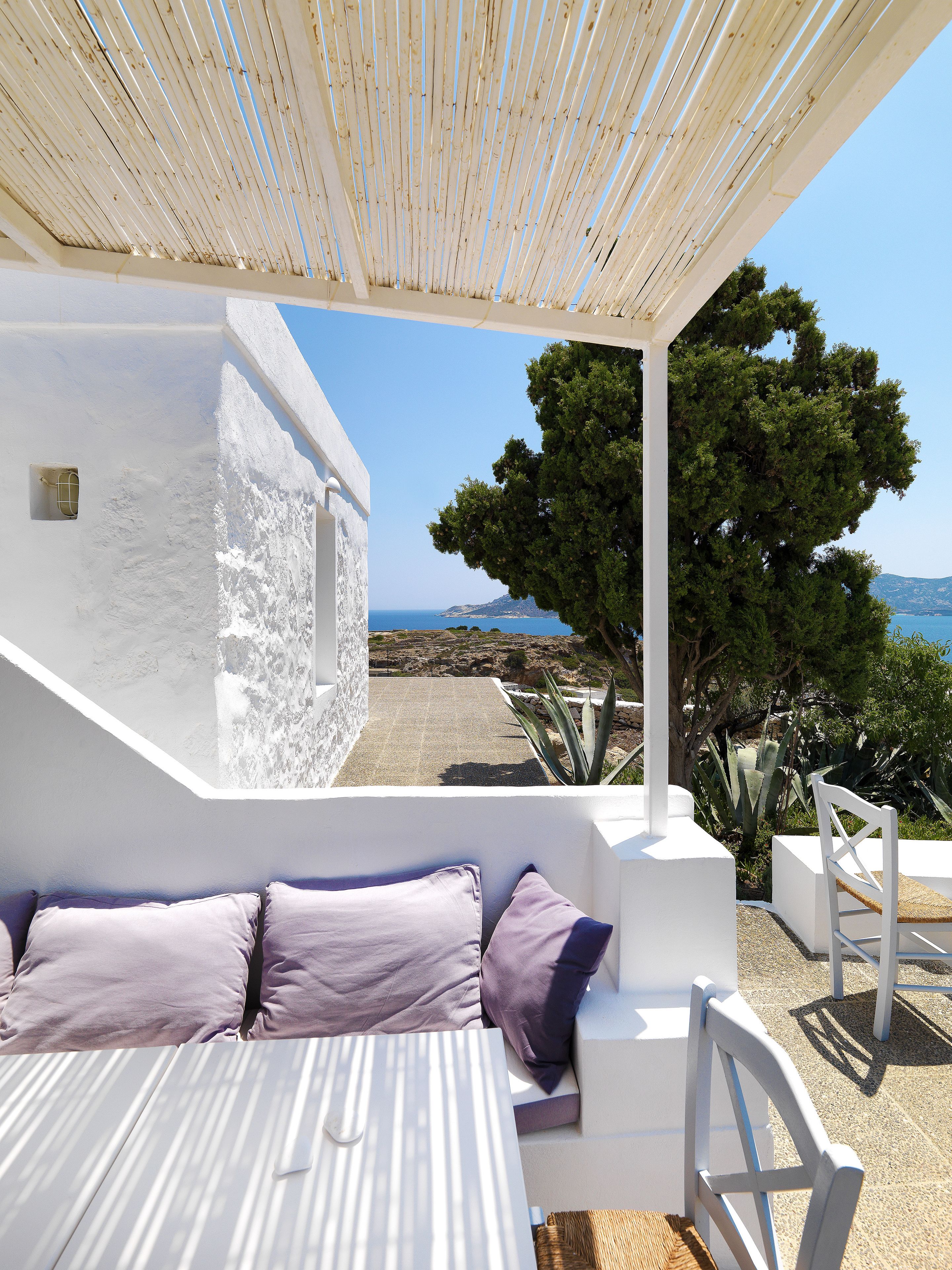 Un área de estar exterior blanca con vistas al mar y un árbol.