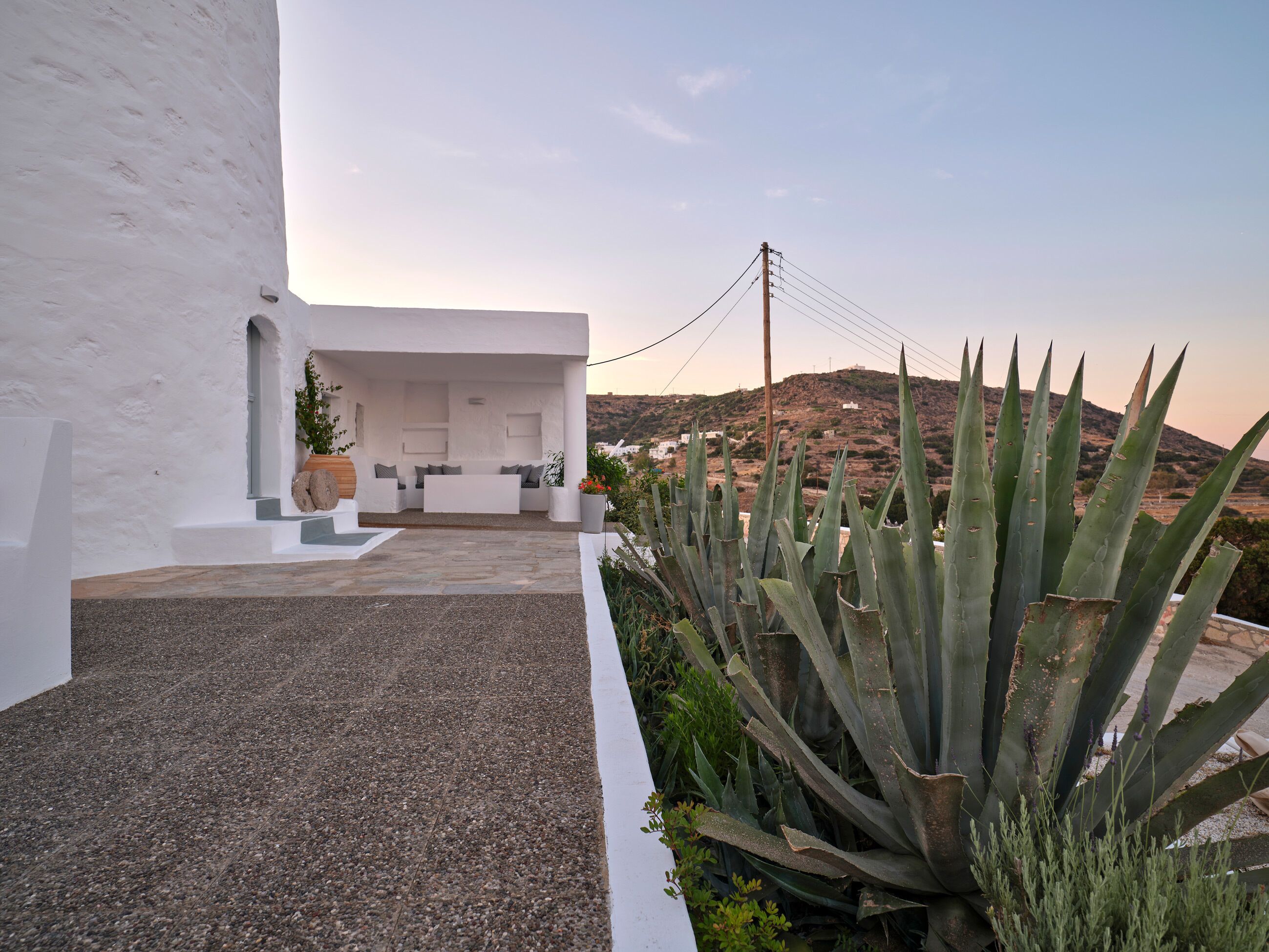 A white building with a patio area, a seating arrangement, and a view of a hill with vegetation.