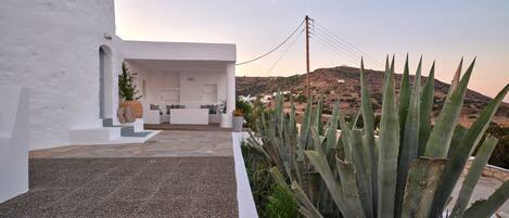 A white building with a patio area, a seating arrangement, and a view of a hill with vegetation.