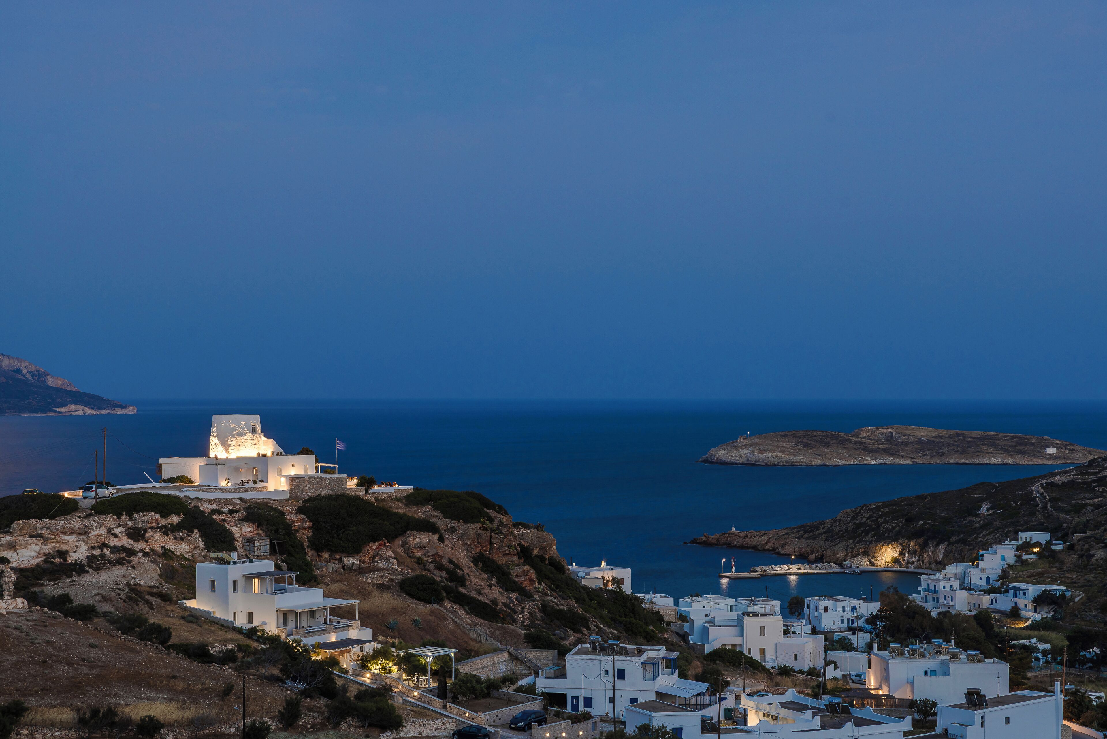 Un pueblo costero con edificios blancos, una estructura destacada con una luz en la parte superior y vistas al mar.