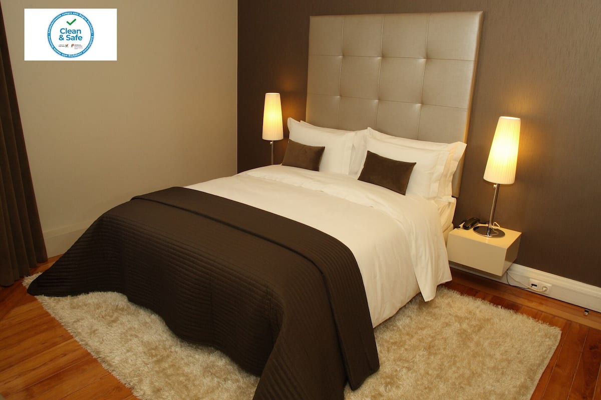A neatly made bed with a tufted headboard, two bedside lamps, and a fluffy rug on a wooden floor.