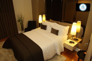 A neatly made bed with white and brown bedding, two bedside lamps, a small table with a phone, and a plant in the corner. - Castilho House (Lisbon)