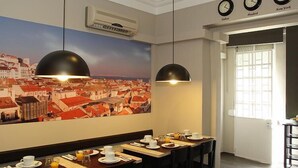 A dining area with a cityscape painting, pendant lights, and clocks displaying times in Madrid and New York. - Castilho House (Lisbon)