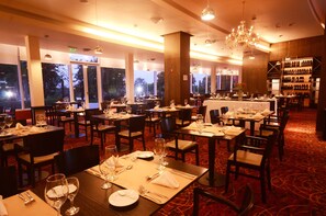 Un restaurant avec de nombreuses tables dressées pour le service, de grandes fenêtres et un lustre.