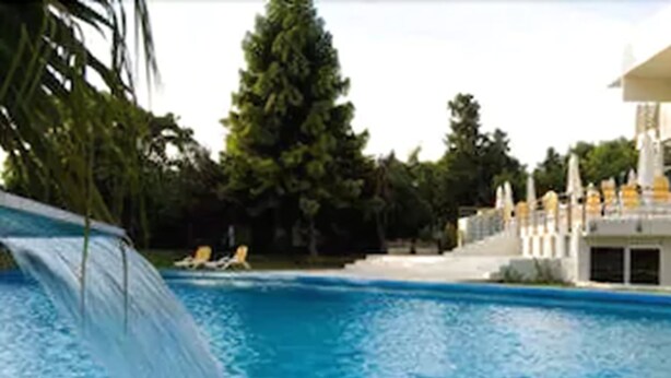 Una piscina con tobogán, sillas de descanso y un edificio de fachada blanca.