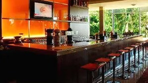 Una barra con una larga encimera, varios taburetes y estantes llenos de botellas.