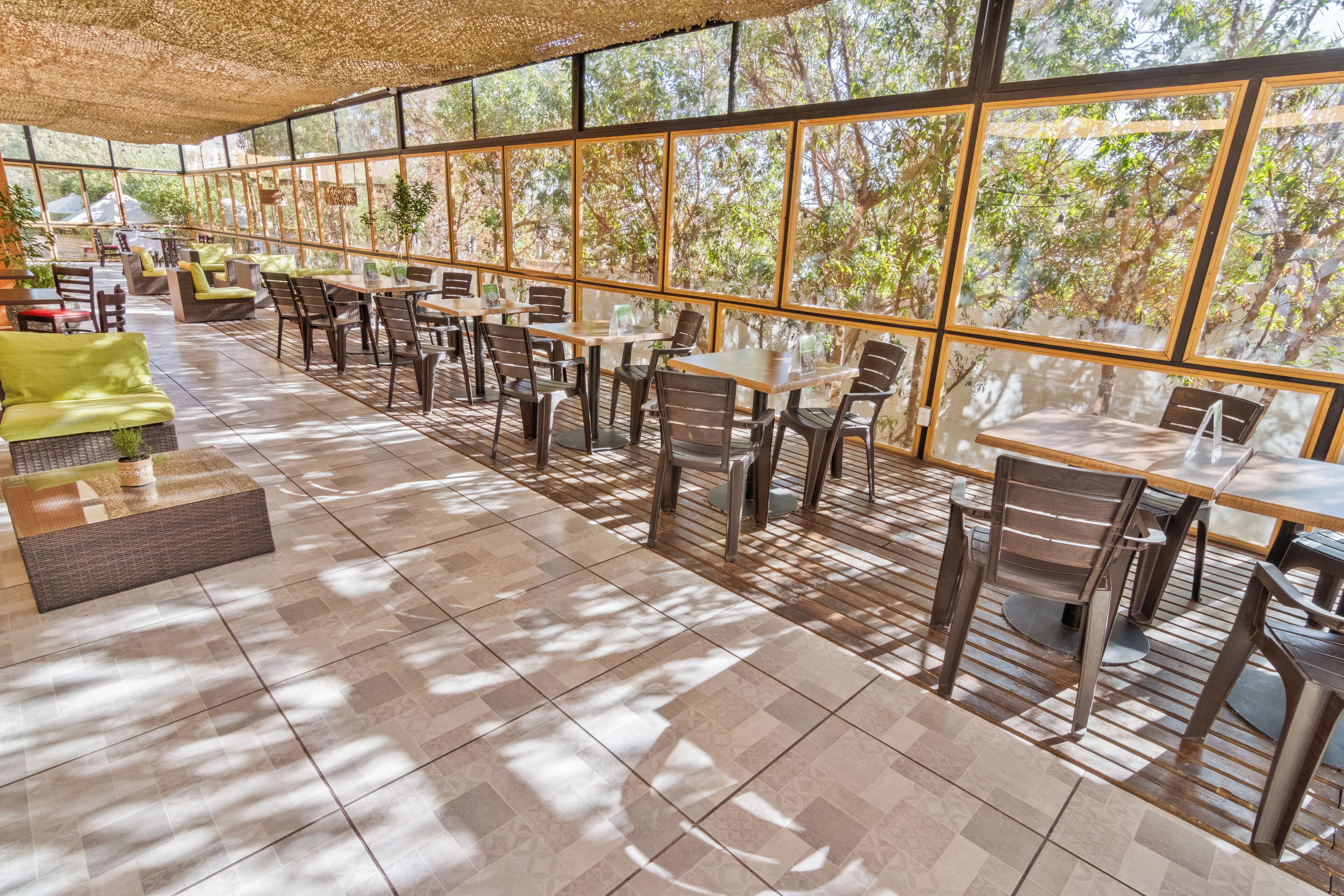 A spacious outdoor seating area with tables and chairs, large windows, and a view of trees.
